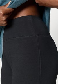 Fekete leggings rugalmas anyagból készülnek, magas derékkal és sima felülettel rendelkeznek, a varrás mentén finom részletekkel.