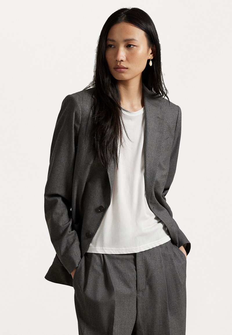 Gray tailored blazer with two buttons, paired with a white t-shirt and matching gray trousers. Smooth fabric with subtle texture details.