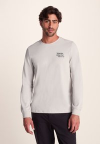 Light gray long-sleeve shirt made from cotton, featuring a round neck and logo accents on the left chest. Soft texture and casual fit.