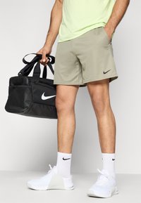 Μαύρο σάκος Nike, ανοιχτό πράσινο αθλητικό πουκάμισο, μπεζ σορτς, λευκά παπούτσια Nike και λευκές κάλτσες με μαύρο λογότυπο.