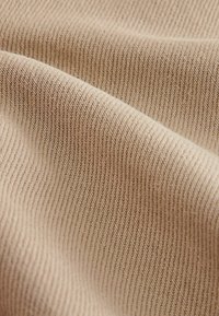 Beige ribbamainen kangas, jossa on hienot pystysuorat viivat, pehmeä rakenne ja pieni kiilto, joka esittelee tasaisen, kudotun ulkonäön.