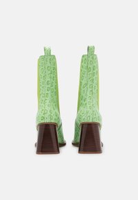 Botines verdes con textura de cocodrilo, que cuentan con un tacón grueso similar a la madera y paneles laterales elásticos para facilitar su uso.