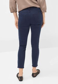 Marineblaue Slim-Fit-Jeans mit glatter Textur und zwei Gesäßtaschen, kombiniert mit schwarzen Mesh-Schlüpfschuhen.