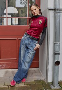 Maroon krievijas futbols t-krekls ar melniem akcentiem, kopā ar brīviem ziliem džinsiem. Melna kniedēta josta un sarkani kedas papildina šo izskatu.