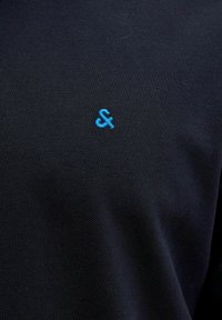 Námornícky polo tričko s jemne textúrovanou látkou a malým modrým logom na hrudi. Dizajn je jednoduchý a klasického štýlu.