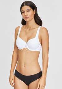 Weißer BH mit Unterwäsche und breiten Trägern sowie einem zentralen Schleifendetail, kombiniert mit schwarzen Slips mit Spitzenverzierung, die kontrastierende Farben und Texturen betonen.