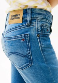 Jeans de mezclilla azul claro con una etiqueta de cuero etiquetada "TOMMY HILFIGER" en la cintura, que cuenta con dos bolsillos traseros y costuras en contraste.