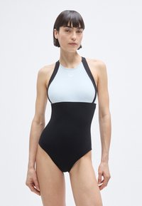 Μαύρο και ανοιχτό μπλε μαγιό, με ψηλό λαιμόκοψη, σχεδιασμό racerback και κομψή, λεία υφή. Αντιθετικά χρώματα τονίζουν τις γραμμές του σχεδίου.