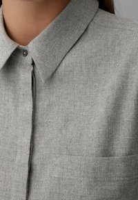 Grijze button-up shirt met een puntige kraag, gemaakt van gestructureerde stof, met een enkele zak en subtiele stikdetails.