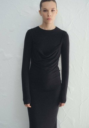 Vestido negro de manga larga en tela elástica, con diseño frontal drapeado y silueta ajustada, de textura suave y detalles mínimos.