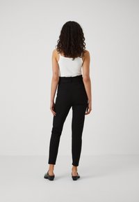 Černé kalhoty na míru se slim fit střihem a vysokým pasem. Mají zadní kapsy a hladkou strukturu. Nosí se s bílým tílkem.