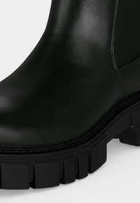Gros plan sur l'avant et la semelle d'une botte en cuir noir avec une semelle crantée et des coutures visibles le long du bord.