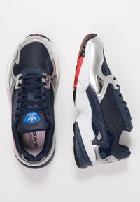 Marinblå och silver sportskor med mesh-material, plastdetaljer, texturerad sula och distinkta färgdetaljer i röd och vit.