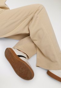 Beżowe bawełniane spodnie o prostym kroju, w połączeniu z białymi sneakersami z czarnym paskiem i teksturowaną brązową gumową podeszwą.