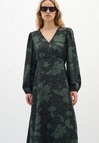 Lång grön klänning med V-ringning, långa puffärmar och ett blommönster i m�örkgrön och svart. Mjuk textur, midilängd.