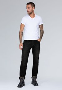 Camiseta de algodón blanca con cuello en V combinada con pantalones vaqueros ajustados negros. Botas de cuero negras con cordones azules. Diseño sencillo y colores sólidos.