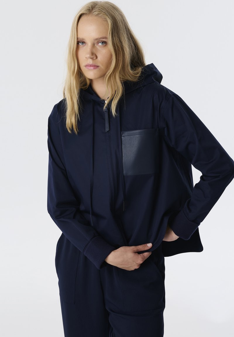 Sudadera con capucha azul marino con un bolsillo frontal, puños acanalados y una textura suave. Presenta una cremallera en el cuello y un ajuste relajado.