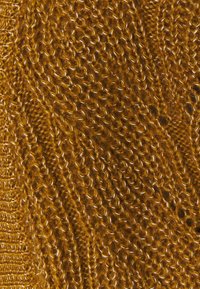 Neulottu kangas rikkaassa kultaharmaassa, jossa on teksturoitu kuvio, jossa on kierrettyjä ja silmukoituja ompeleita, korostaen pehmeyttä ja lämpöä.