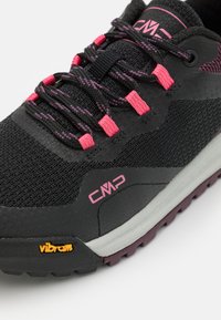 Zapato de senderismo negro con detalles en gris, con parte superior texturizada, cordones rosas y logo de Vibram naranja en la suela. Diseño robusto y funcional.
