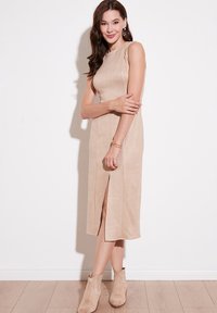 Tan sävyinen samettinen midi-mekko, jossa on korkea kaulus, sivuaukko ja tiukka leikkaus. Asusteena beige nilkkurit ja yksinkertainen kultaketju.