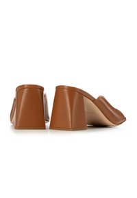 Mules de piel marrón con tacón cuadrado, de textura suave y forma angular. El tacón es de un color sólido con la parte trasera redondeada.