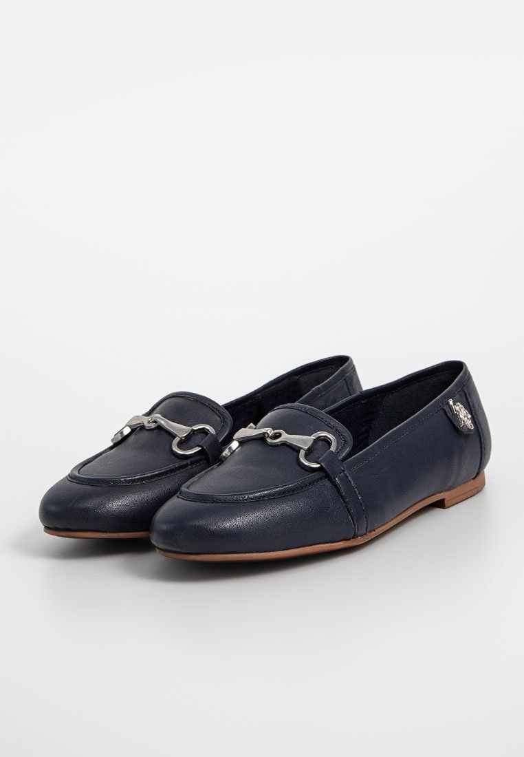 Mocasines de cuero azul marino con un acento de cadena plateada, suela plana y textura suave. Presentan un sutil detalle de logo en el lateral.