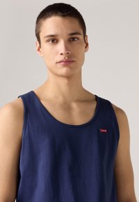Tumedat sinise puuvilla tank-top ümara kaelusega, mille vasakus ülanurgas asub väike punane Levi's logo. Lihtne disain ja kerge tekstuur.