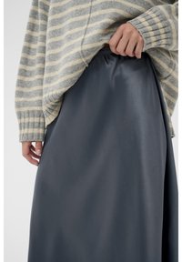 Un pull rayé gris et crème en tissu doux, associé à une jupe lisse gris foncé avec une taille élastique.