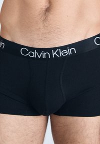 Schwarze Baumwoll-Boxershorts mit weißem Calvin Klein-Logo am Bund. Sie bieten eine enganliegende Passform, eine glatte Textur und keine sichtbaren Muster oder Akzente.