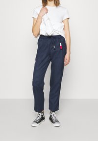 Granatowe, w paski spodnie z elastycznym paskiem w talii, kieszeniami bocznymi i małą metką. W zestawie z białą koszulką i czarnymi trampkami za kostkę.