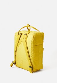 Gul tygryggsäck med vadderad form, justerbara remmar och framficka. Har ett handtag på toppen och tryckknappar för stängning.