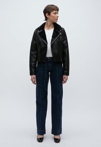 Μαύρο δερμάτινο cropped μπουφάν με γούνινο γιακά, λευκό πουκάμισο, ψηλόμεσο μπλε τζιν και μαύρα παπούτσια από δερμάτινο λουστρίνι.