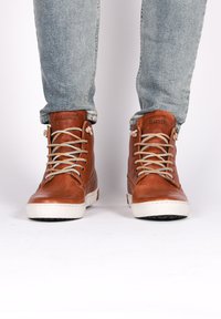 Zapatos de altura alta de cuero marrón con acabado texturizado, suela de goma crema y cordones claros. Logo visible en el lado exterior del tobillo.