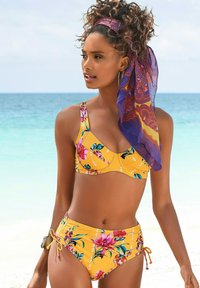 Ensemble de bikini floral jaune comprenant un haut bralette à bretelles ajustables et un bas taille haute, agrémenté de liens et d'une écharpe à motifs.