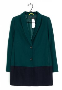 Manteau en mélange de laine, présentant une partie supérieure verte et une partie inférieure bleu marine foncé, avec une fermeture à bouton unique et un col à revers cranté, suspendu à un crochet.