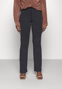 Calças pretas ajustadas com corte direito, feitas de um tecido macio, combinadas com uma blusa de manga longa texturizada em cor ferrugem.