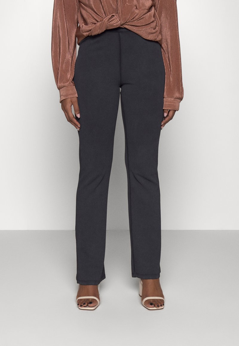 Calças pretas ajustadas com corte direito, feitas de um tecido macio, combinadas com uma blusa de manga longa texturizada em cor ferrugem.