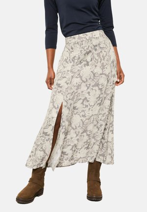 Lang geschnittenen Rock mit floralem Muster in hellem Creme und grauen Details, ausgestattet mit einem Seitenschlitz und hoher Taille. Kombiniert mit braunen kniehohen Stiefeln.