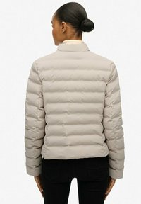 Beige donzen jack met een doorgestikt ontwerp, voorzien van een hoge kraag en lange mouwen. Gladde, glanzende stof met ritssluiting details.