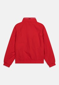 Rode lichtgewicht jas met een kraag, elastische tailleband en manchetten. Aan de achterkant staat het "TOMMY HILFIGER" logo.