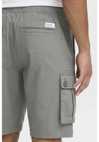 Grau Cargo-Shorts mit einem Kordelzugbund, seitlichen und hinteren Taschen sowie einer Knopfverschlussklappe. Hergestellt aus leichtem Stoff mit einer glatten Textur.