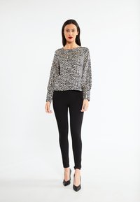 Langærmet top i leopardmønster lavet af blødt stof, parret med tætsiddende sorte leggings og sorte spidse hæle. Enkel, moderne design.