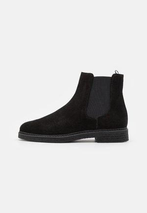 Bottine en daim noir avec panneau latéral élastique et talon bas superposé, conçue pour un enfilage facile et un confort optimal.