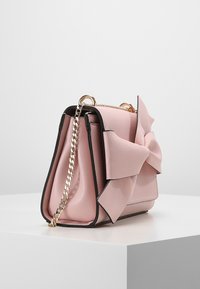 Różowa skórzana torebka z wyraźnym detalem w postaci kokardy, czarnym wykończeniem i złotym łańcuszkiem. Posiada sztywny kształt i teksturowane wykończenie.