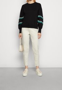 Czarny sweter z turkusowymi frędzlami na rękawach, w zestawieniu z kremowymi dżinsami i białymi trampkami. W komplecie mała torebka o teksturowanej powierzchni.