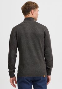 Dark gray knit sweater with a high collar and ribbed cuffs. Features elbow patches and a textured finish. The hem includes a small label.