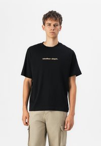 Schwarzes Baumwoll-T-Shirt mit kurzen Ärmeln, Rundhalsausschnitt und "atelier dept." in Gold auf der Brust gedruckt. Schlicht, entspannter Schnitt.