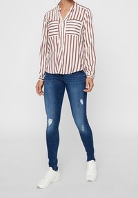 Vit blus med vinröda vertikala ränder, två bröstfickor, ihop med mörkblå skinny jeans med slitna detaljer och vita sneakers.