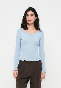 Ανοιχτό μπλε ριμπ μακρυμάνικο τοπ με στρογγυλή λαιμόκοψη και βολάν στο τελείωμα. Κατασκευασμένο από μαλακό πλεκτό ύφασμα, διαθέτει εφαρμοστά μανίκια και διακριτική υφή.