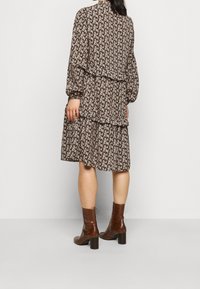 Svart blommig klänning med långa ärmar, lagerdesign och bruna ankelskor med texturerad finish. Ljust röda blommor kontrasterar mot den mörka bakgrunden.